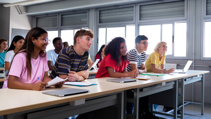 Panoramic image of multiracial happy, smiling college students in classroom listening to lecture.