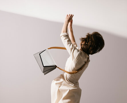 Woman In Beige Dress With Flying Handbag Posed Dramatically
