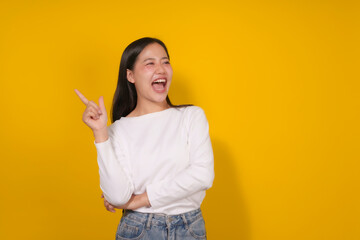 Young woman is pointing her finger and laughing while standing on a yellow background