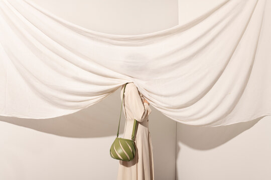Person Peeking Through White Drapes with Green Bag