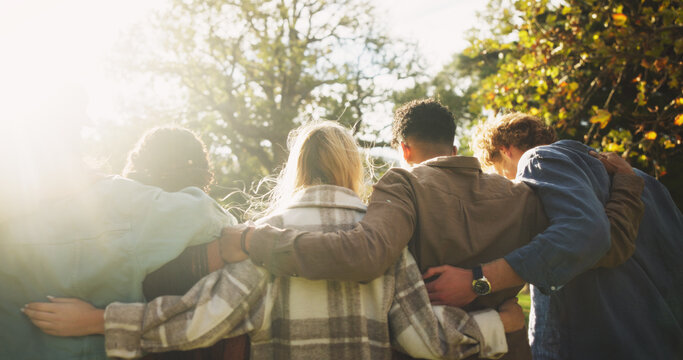 Group, back and friends to relax outdoor on school break, lens flare and hug for bonding in summer. People, students and embrace with support, care and trust together for social reunion at park - Powered by Adobe