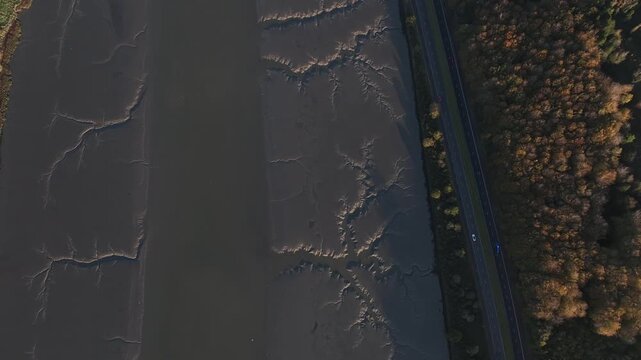 Flagstaff, County Down, Northern Ireland, November 2022. Drone in Bird's Eye view ascends above the Newry river as cars drive along the A2 Warrenpoint Road during the early morning.