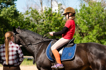 Child rider adjusts position on horse under instructor's watch.