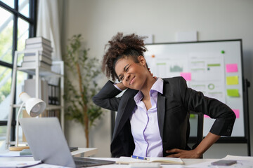 Stressed businesswoman at desk with neck pain from laptop work, highlighting importance of...