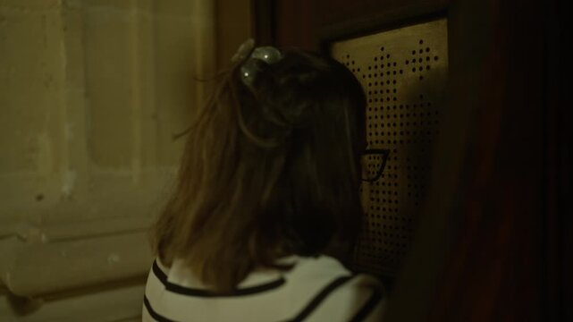 A young woman is seen inside an italian church engaging with a confessional booth, highlighting her christian faith and devotion in a solemn, sacred setting.
