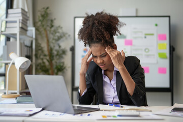 Young manager woman feeling tired and having a bad headache while working with laptop computer in the modern office