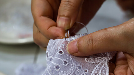 Closeup of an Indonesian woman's hands making or sewing a traditional white kebaya. It highlights the cultural craftsmanship, showcasing elegant lace patterns and meticulous attention to detail