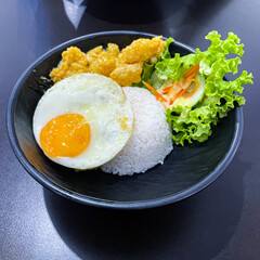 rice bowl with salted fried dory fish and egg served with salad in black bowl