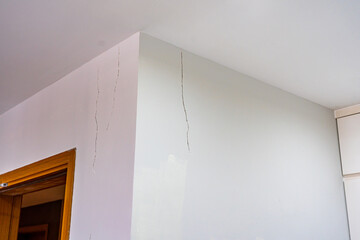 White painted wall with cracks near the ceiling 