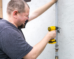 A man is using a drill to fix a pipe