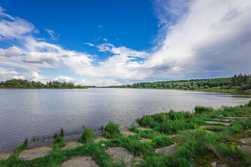 A peaceful lake reflects the vibrant sky, framed by verdant grasses and trees, creating a serene...