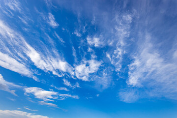 Fototapeta premium Wispy clouds gracefully float through a brilliant blue sky, creating a serene and picturesque view under the glow of midday sunlight.
