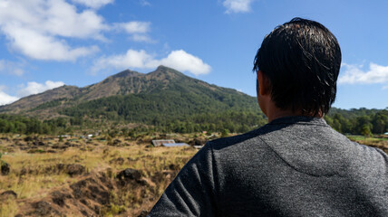 Back view of a male tourist or traveler looking at Mount Batur in Bali, Indonesia. Beautiful view under a clear sky, perfect for travel and nature themes, highlighting adventure and exploration