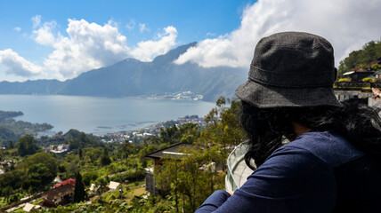 Back view of a tourist couple looking at Batur Lake and Trunyan Hill in Bali. The couple enjoys the scenic view, highlighting the natural beauty of the landscape. Travel and nature photograpy concept