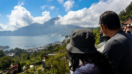 Back view of a tourist couple looking at Batur Lake and Trunyan Hill in Bali. The couple enjoys the scenic view, highlighting the natural beauty of the landscape. Travel and nature photograpy concept