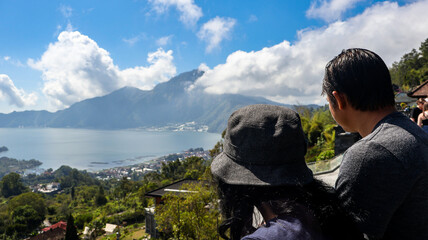 Back view of a tourist couple looking at Batur Lake and Trunyan Hill in Bali. The couple enjoys the scenic view, highlighting the natural beauty of the landscape. Travel and nature photograpy concept