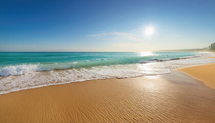 Obraz premium A serene beach scene with gentle waves lapping the golden sand, under a clear blue sky and bright sun.