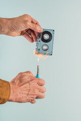 Male meloman burning old audio tape cassette on blue background. Audio cassette and lighter, illustrating the process of destruction and disposal through ignition and burning