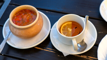 A bowl of soup and a cup of tea sit on a table. The table is made of wood and has a wooden tablecloth. The scene is cozy and inviting