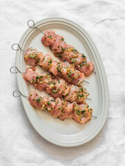 Raw marinated chicken skewers on an oval plate on a light surface