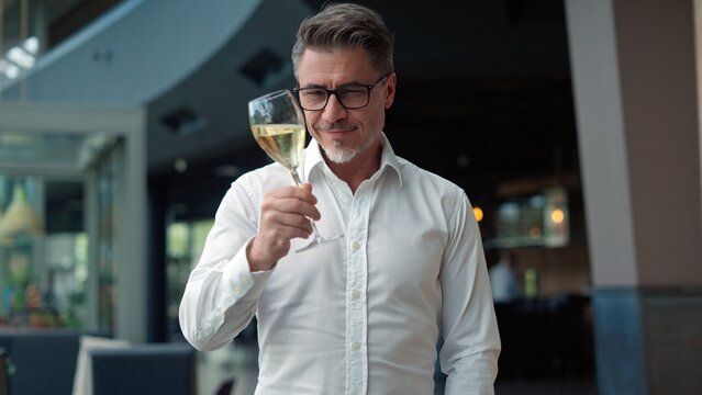 Elegant man tasting glass of white wine in restaurant - Powered by Adobe