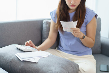 Asian woman holding paper document calculating money savings paying bills in mobile application...