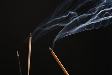 Aromatic incense sticks smoldering on black background