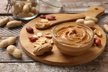 Tasty peanut butter in bowl and groundnuts on wooden table