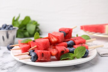 Skewers with tasty watermelon, strawberries, blueberries and mint on white marble table, closeup