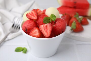 Tasty watermelon and melon balls with strawberries in bowl on white tiled table, closeup