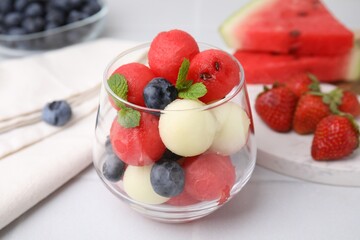 Tasty watermelon and melon balls with blueberries in glass on white table, closeup
