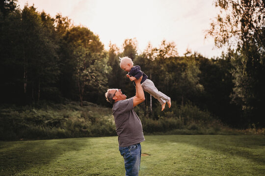 Grandpa holding grandchild in the air in the woods outdoors