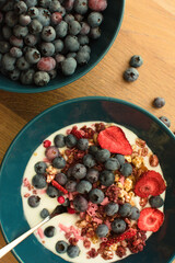Greek yogurt with wholegrain muesl, granola, dried strawberries and fresh blueberries in a blue bowl.