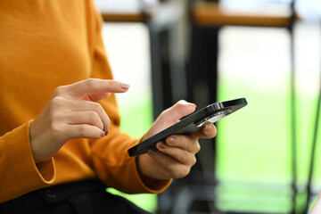 Cropped image of young woman dressed in orange turtleneck sweater using smartphone at office