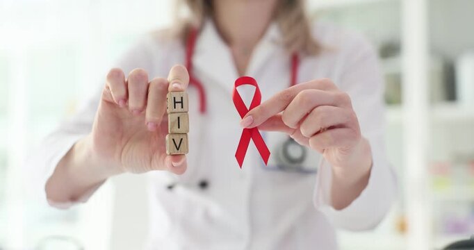 Doctor holding red ribbon and wooden blocks with word HIV closeup.