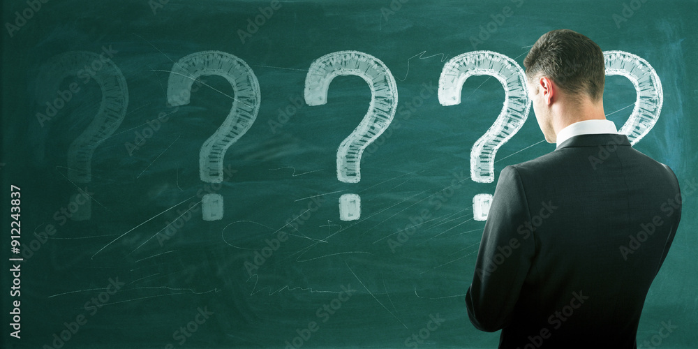 Poster back view of thoughtful young european male with chalk drawn question marks on blackboard background