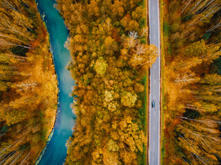 Aerial view of fall color trees woods, blue river and asphalt road with car