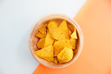 Corn chips on wooden plate isolated on orange and yellow background. Crispy snack dessert. Food Photography Concept
