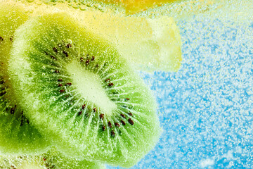 Slices of kiwi and lemon float in sparkling bubbles, creating refreshing and vibrant scene against...