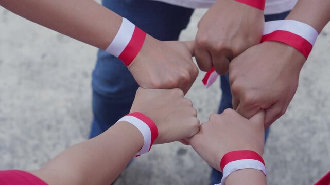 Group of Young People Unite Hand Together Wearing Indonesian Red And White Ribbon On Wrist. Unity Concept