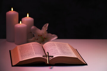 Cross, Bible, flower and burning candles on textured table against black background, space for text. Religion of Christianity