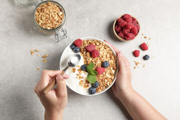 Woman eating tasty granola with berries and yogurt at grey textured table, top view
