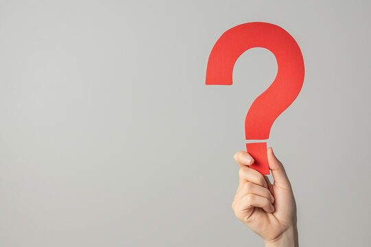 hand holding up a big red question mark made of paper isolated on clean smooth solid background