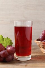 Tasty juice in glass, fresh grapes and leaf on wooden table