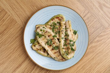 Tasty grilled courgette slices with parsley on wooden table, top view