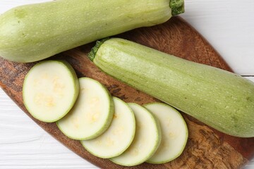 Board with fresh zucchinis on white wooden table, top view