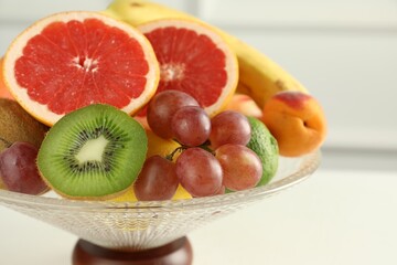 Glass vase with different fresh fruits on white table, closeup