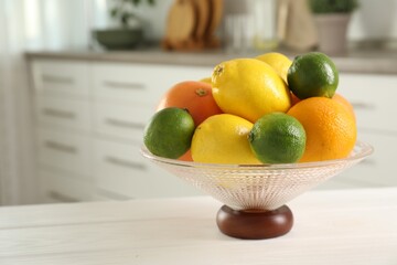 Glass vase with different citrus fruits on white table indoors. Space for text