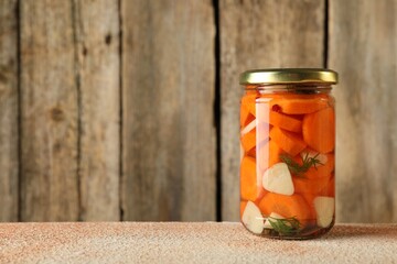 Tasty pickled vegetables in jar on beige textured table, space for text