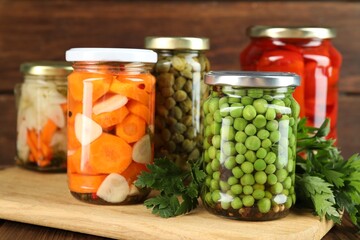 Different pickled products in jars and fresh parsley on wooden table